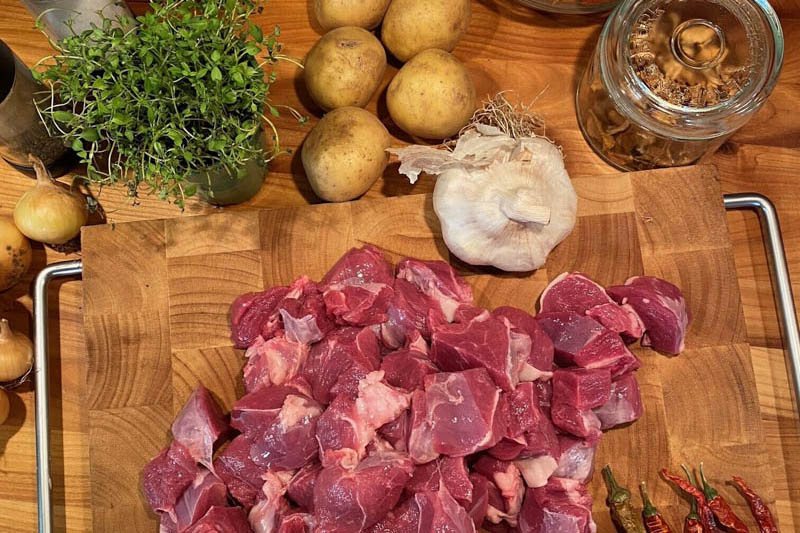 Styckdetaljer av lamm på en skärbräda med potatis, vitlök och timjan